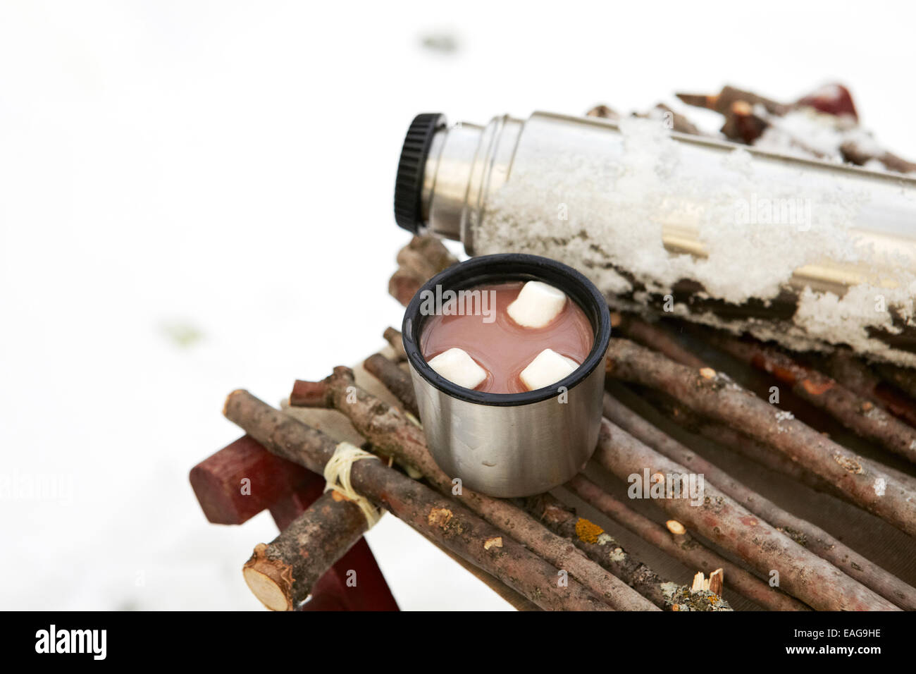 Thermos and cup of Hot Chocolate with marshmallows in winter setting. Stock Photo