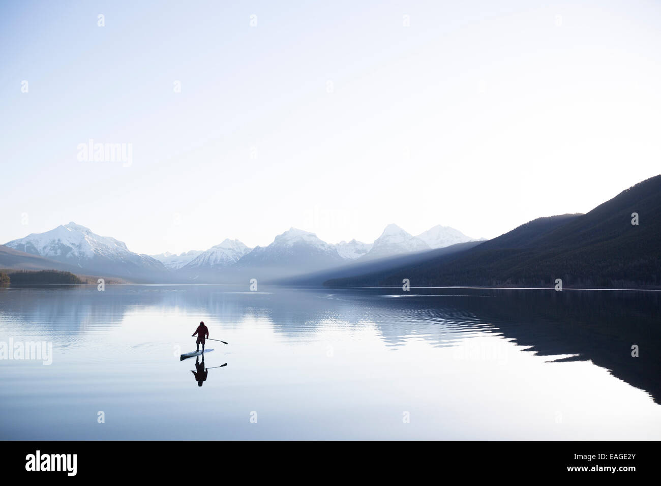 A man stand up paddle boards (SUP) on a calm Lake McDonald in Glacier National Park. Stock Photo