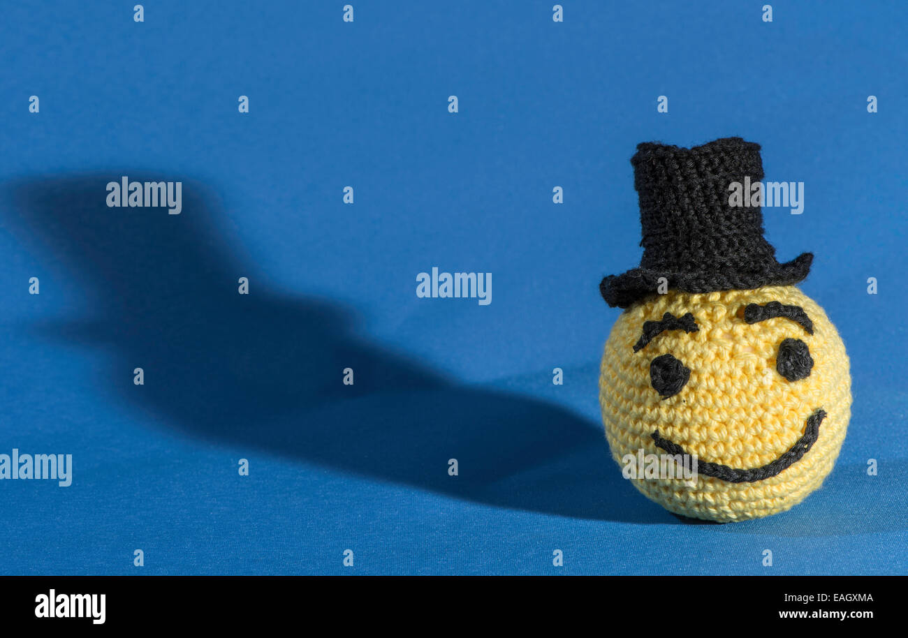 Knitted yellow emoticon with bowler on blue background Stock Photo