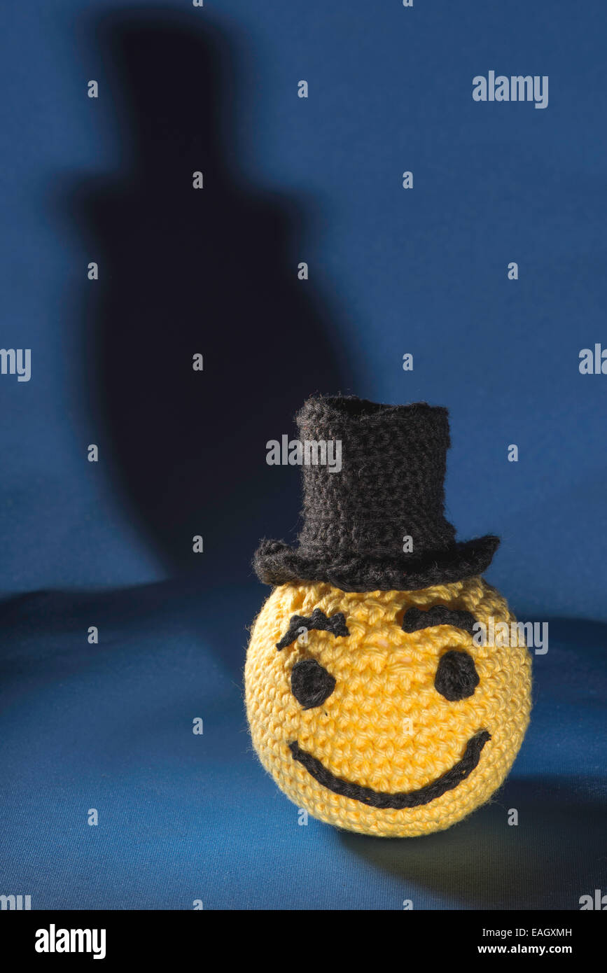 Knitted yellow emoticon with bowler on blue background Stock Photo