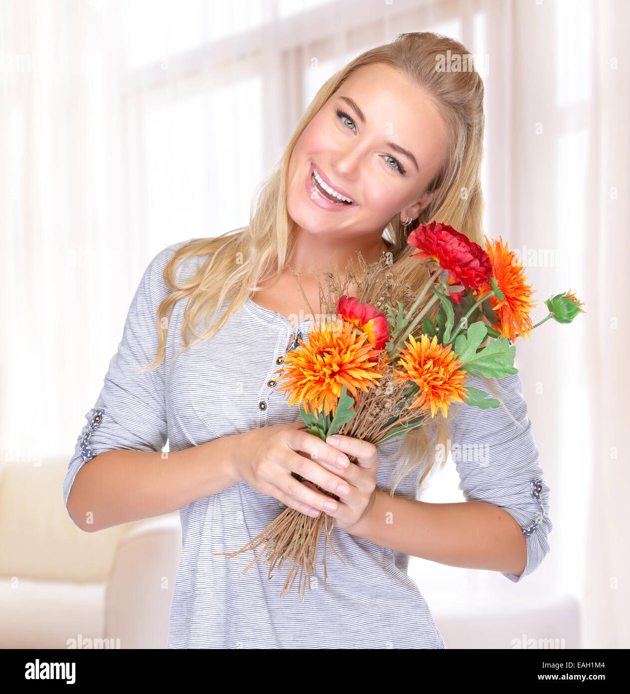 Portrait of cheerful smiling female with flowers bouquet in hands, spending autumn holiday at home, enjoying cute present Stock Photo