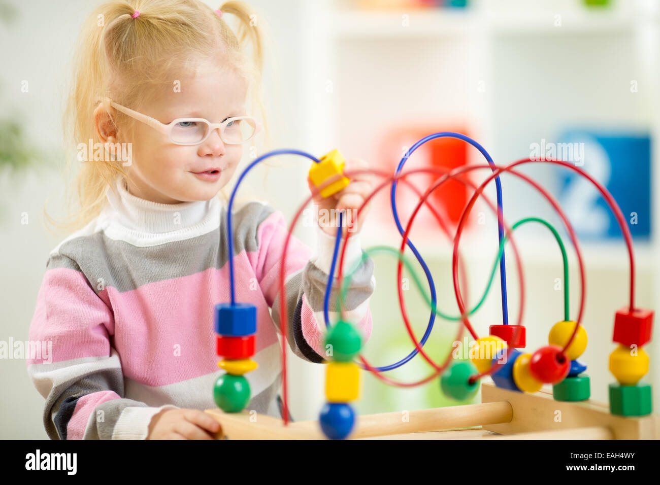 Kid in eyeglases playing colorful toy in home interior Stock Photo