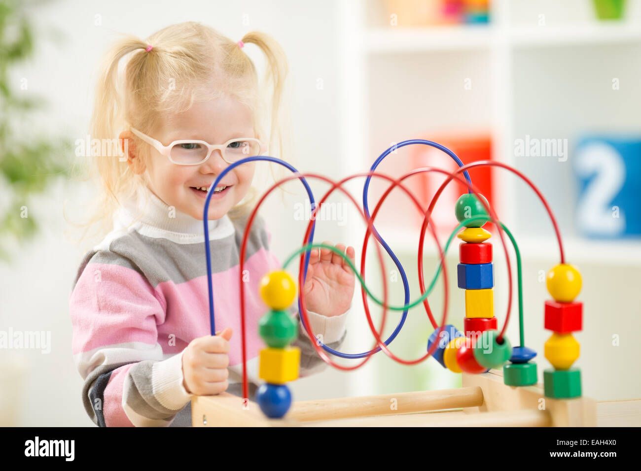 Kid in eyeglases playing colorful toy in home interior Stock Photo