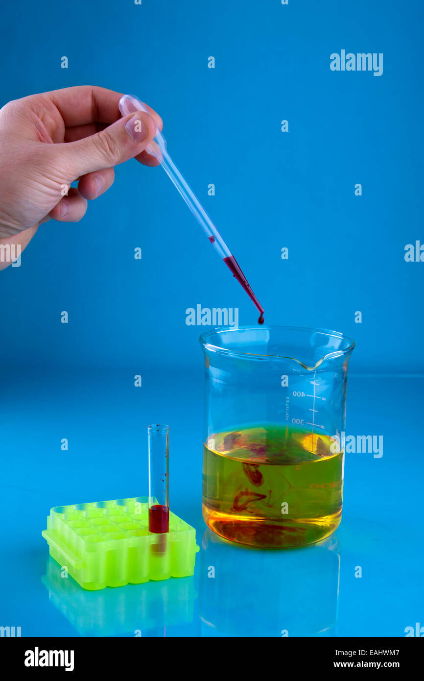 Pipetting red dye into a beaker containing a yellow liquid. Stock Photo