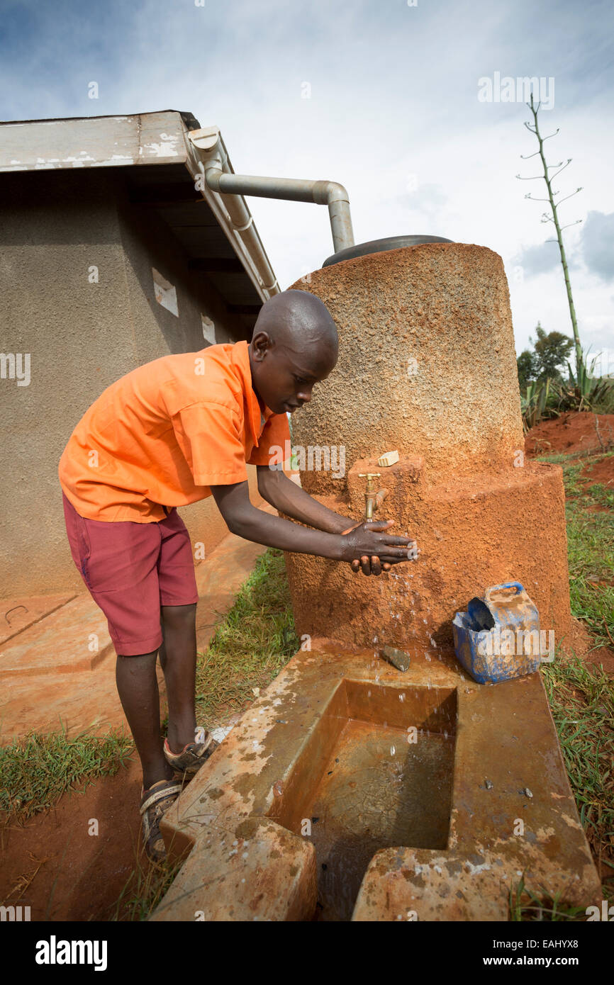 A student washes his hands outside the boys' toilet block at Kaptomologon Primary School in Bukwo, Uganda using water from a rai Stock Photo