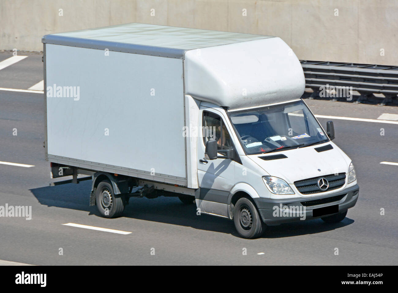 View from above side & front looking down driver in Mercedes Benz white clean unmarked delivery van streamline curved front driving along UK motorway Stock Photo