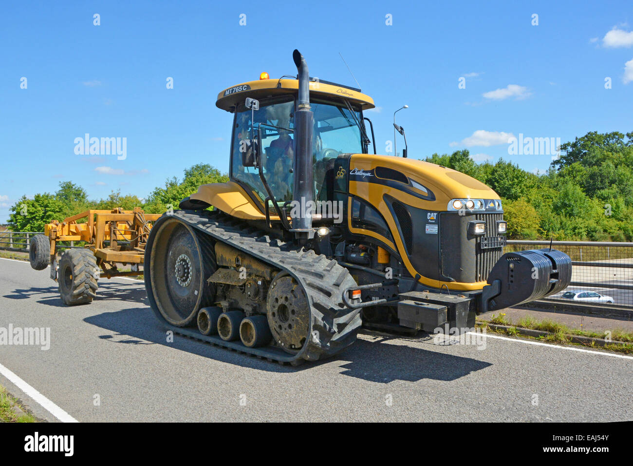 Tracked wide vehicle agriculture Caterpillar Challenger farming tractor driving rural public road bridge crossing above M25 motorway Essex England UK Stock Photo