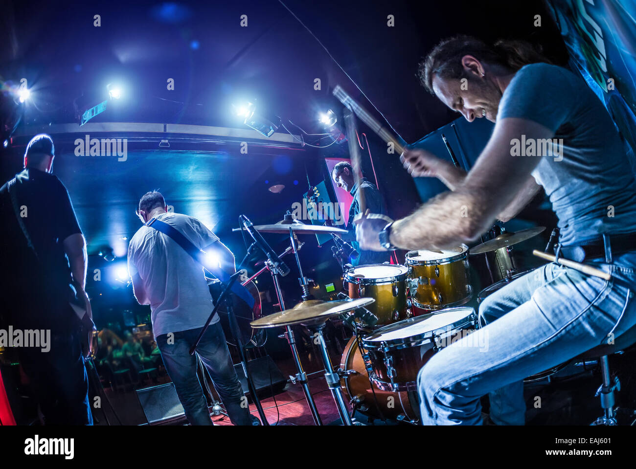 Drummer playing on drum set on stage. Warning - Focus on the drum, authentic shooting with high iso in challenging lighting cond Stock Photo