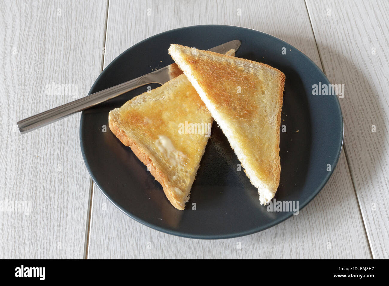 Piece of buttered hot toast, cut into triangles on a plate with a knife