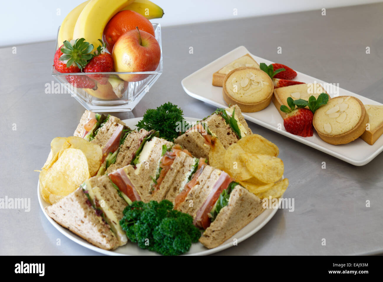 plated buffet lunch with a selection of sandwiches fruit baked sweets and crisps Stock Photo