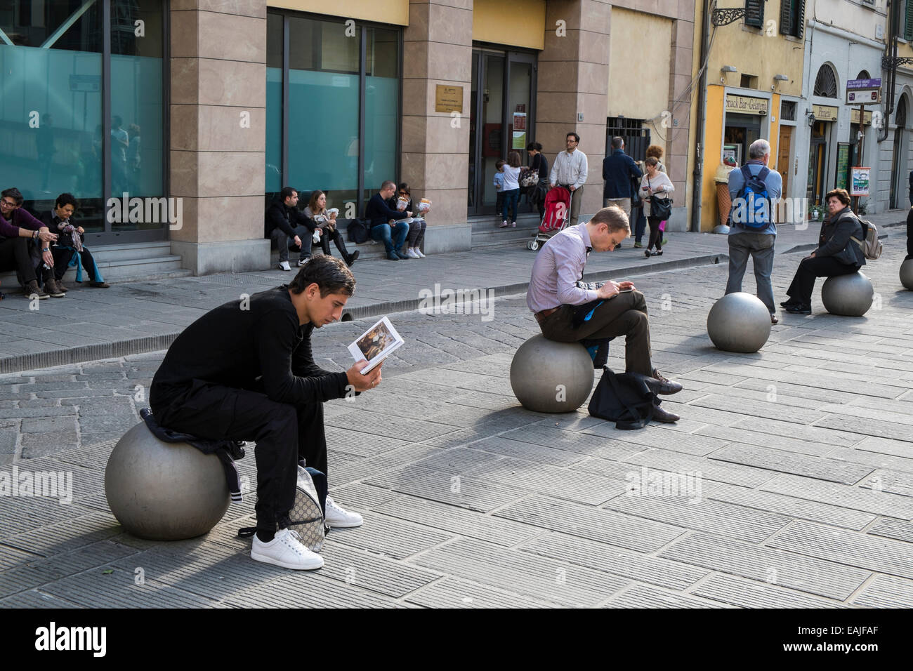 Young man reading on a metal ball in Florence street. Stock Photo