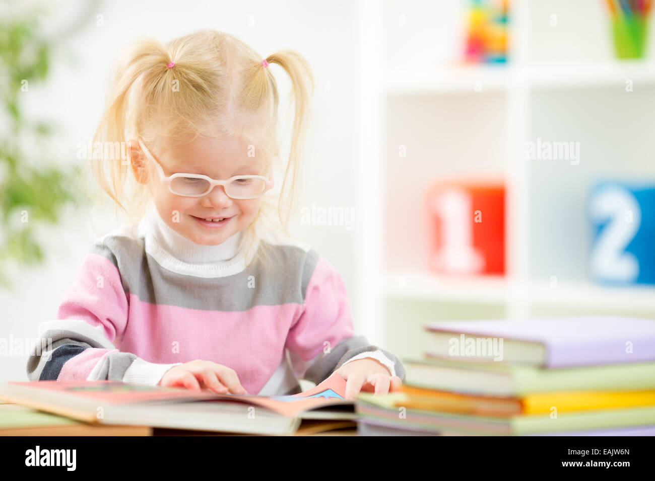 Funny child in eyeglases reading book at home Stock Photo