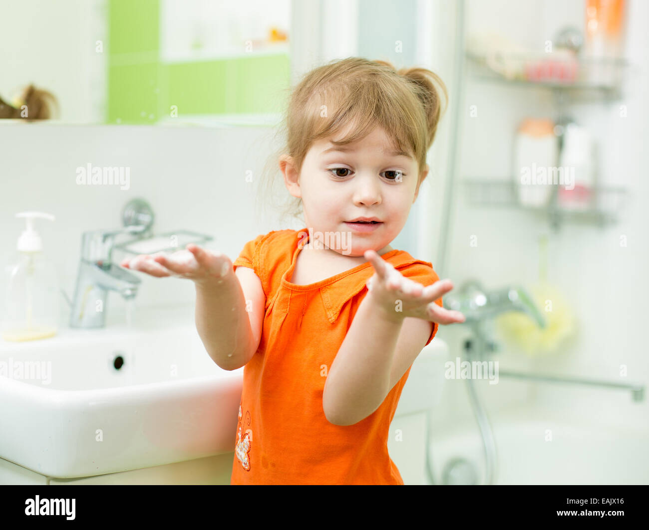 Funny little girl washing hands in bathroom Stock Photo