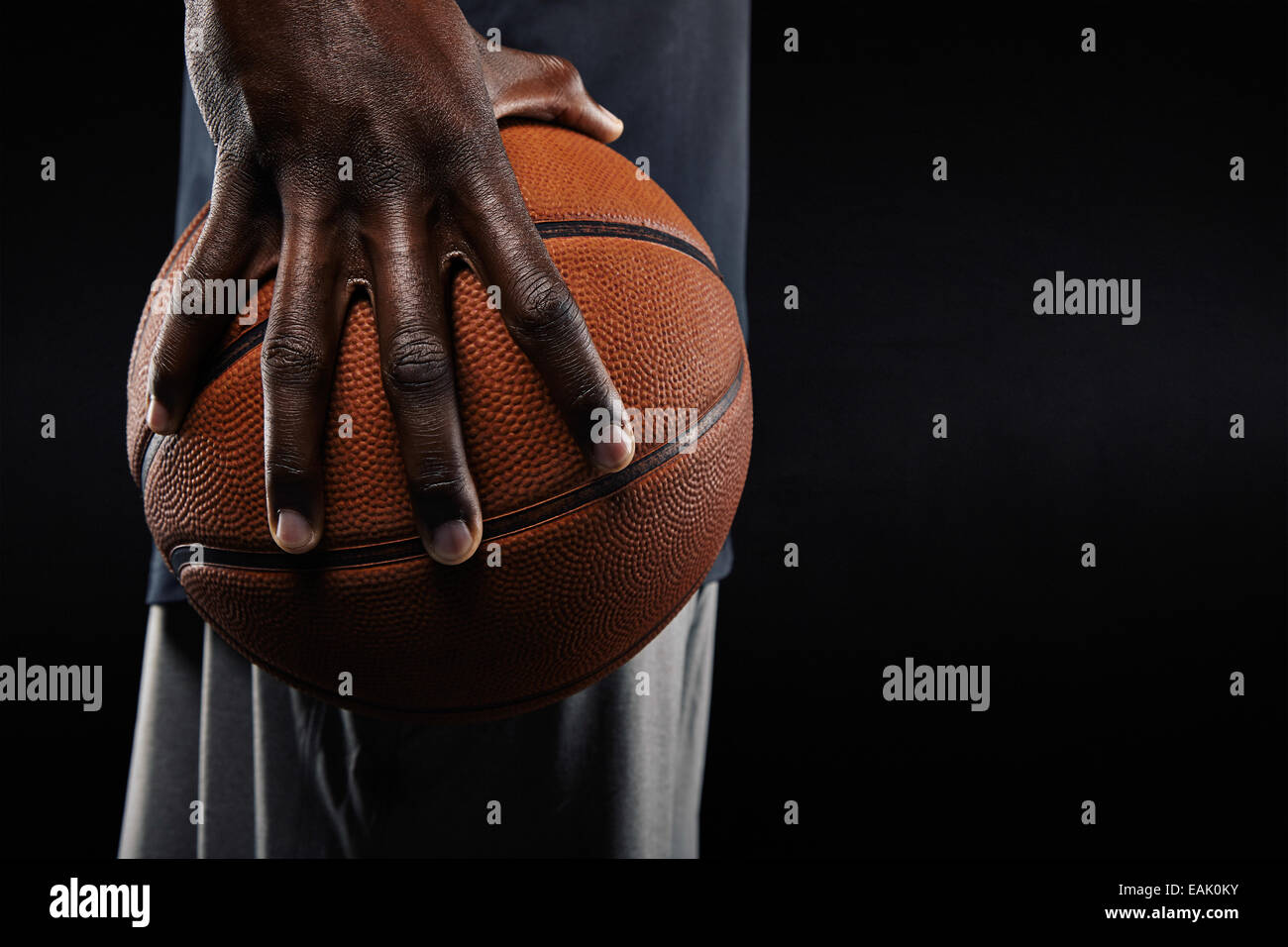 Close-up of a hand of basketball player holding a ball against black background. Stock Photo
