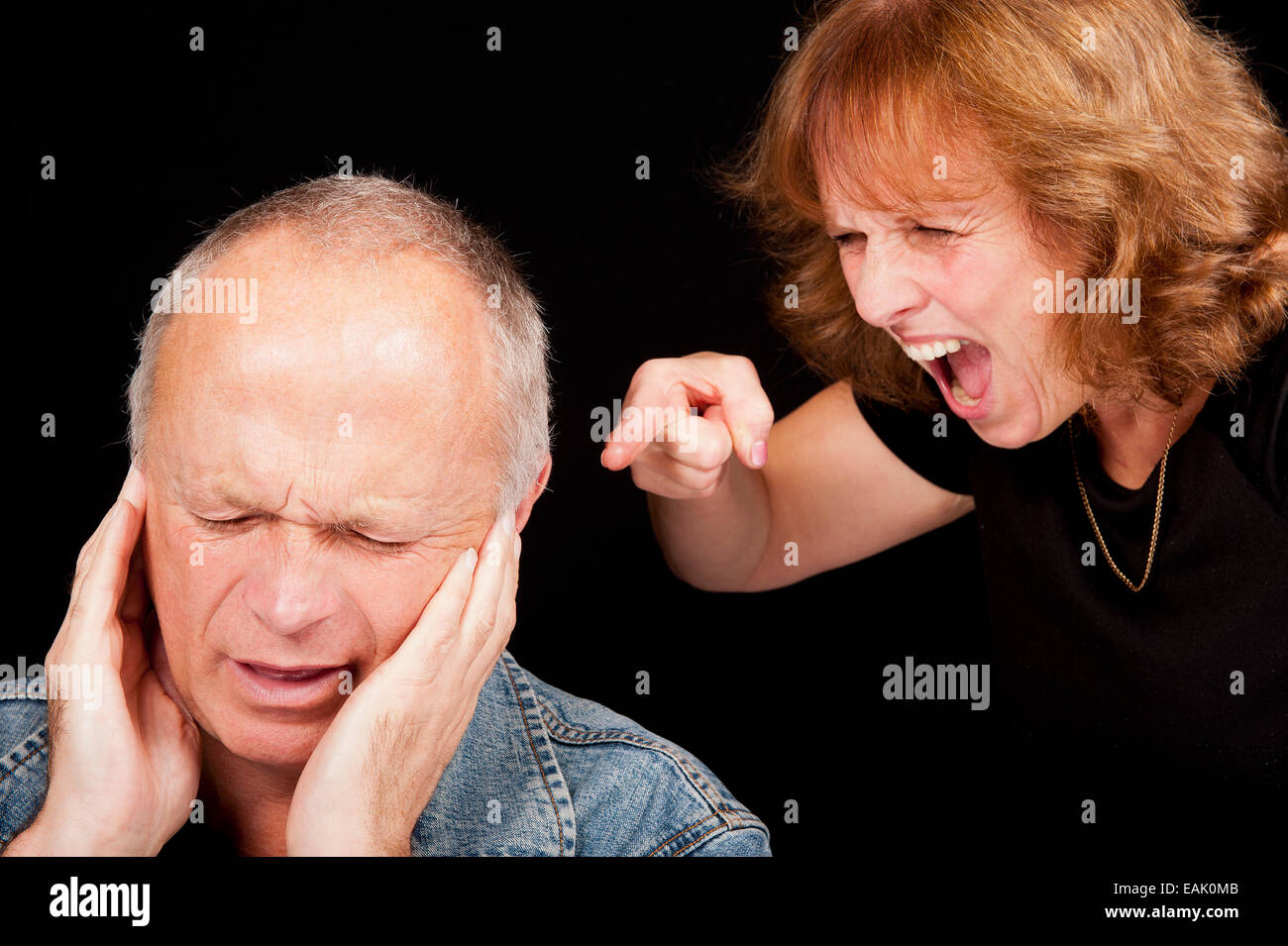 Middle aged couple having an argument, with the woman shouting and pointing finger at the crying man. Stock Photo