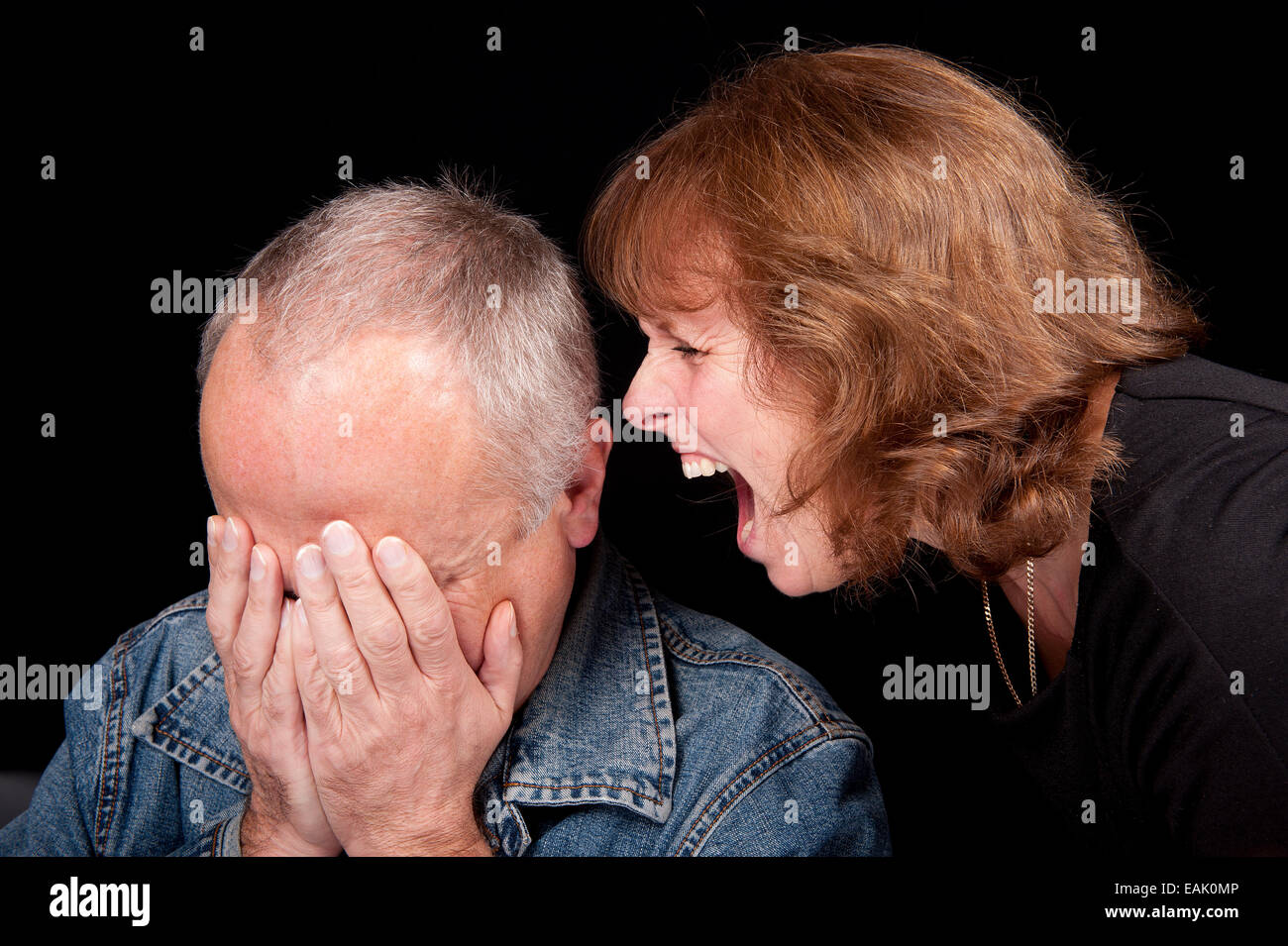 Middle aged couple having an argument, with the woman shouting at the man while he is crying. Stock Photo