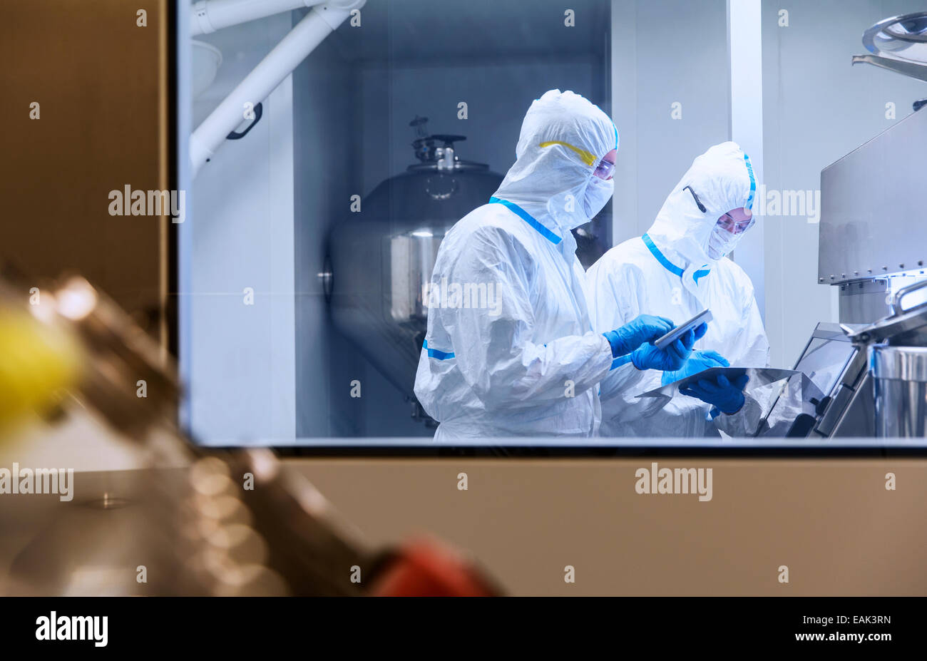 Scientists in clean suits using digital tablets in experiment in laboratory Stock Photo