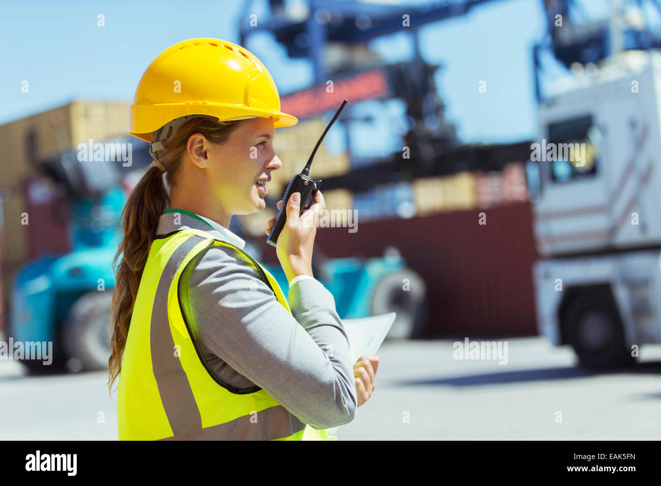 Businesswoman using walkie-talkie near cargo containers and trucks Stock Photo
