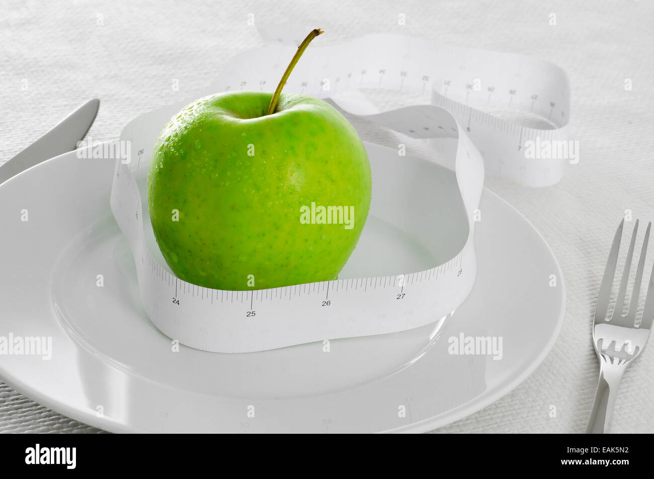closeup of a plate with a fresh apple and a measuring tape on a set table, symbolizing the concept of dieting or to stay fit Stock Photo