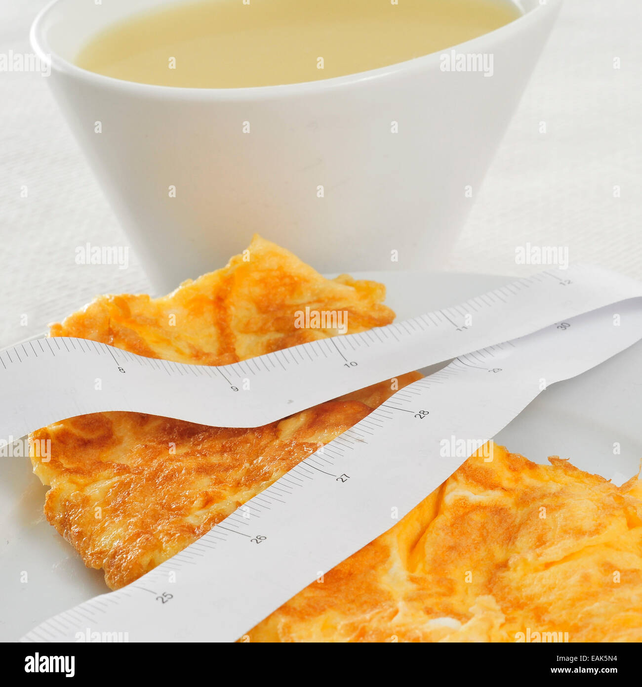 a bowl with consomme and a plate with a french omelette and a measuring tape, symbolizing the dieting concept Stock Photo