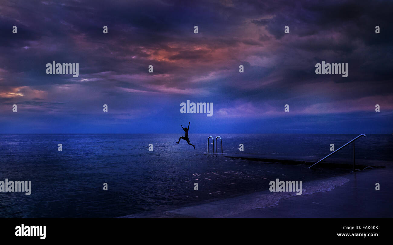 A color landscape photograph of a person in silhouette jumping into the sea in Slovenia, Europe Stock Photo
