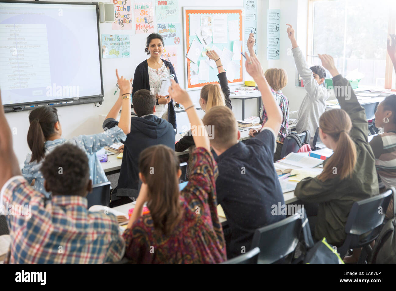 Rear view of teenage students raising hands in classroom Stock Photo