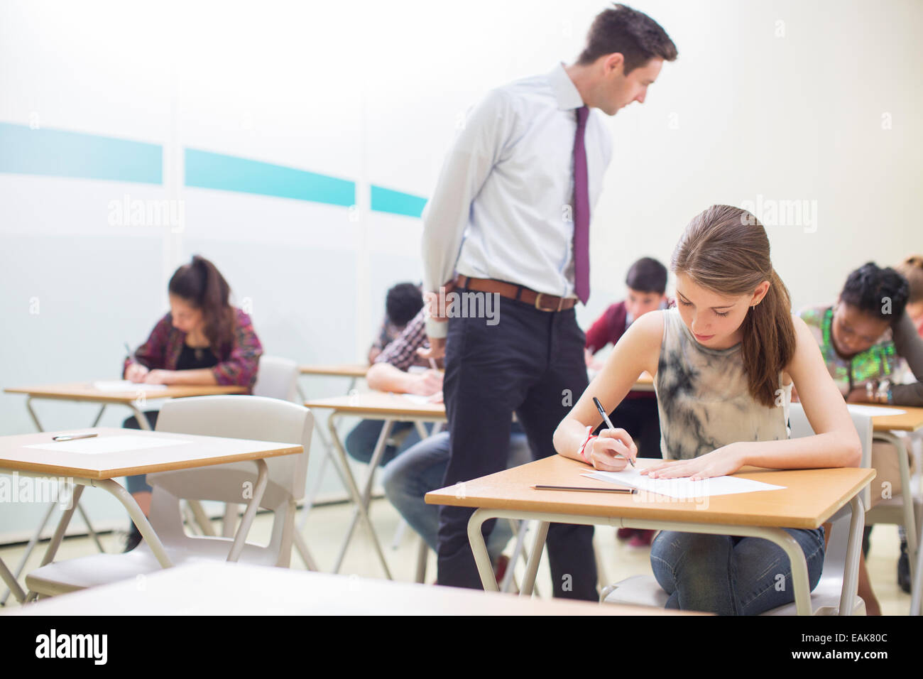 Male teacher supervising students writing their GCSE exam in classroom