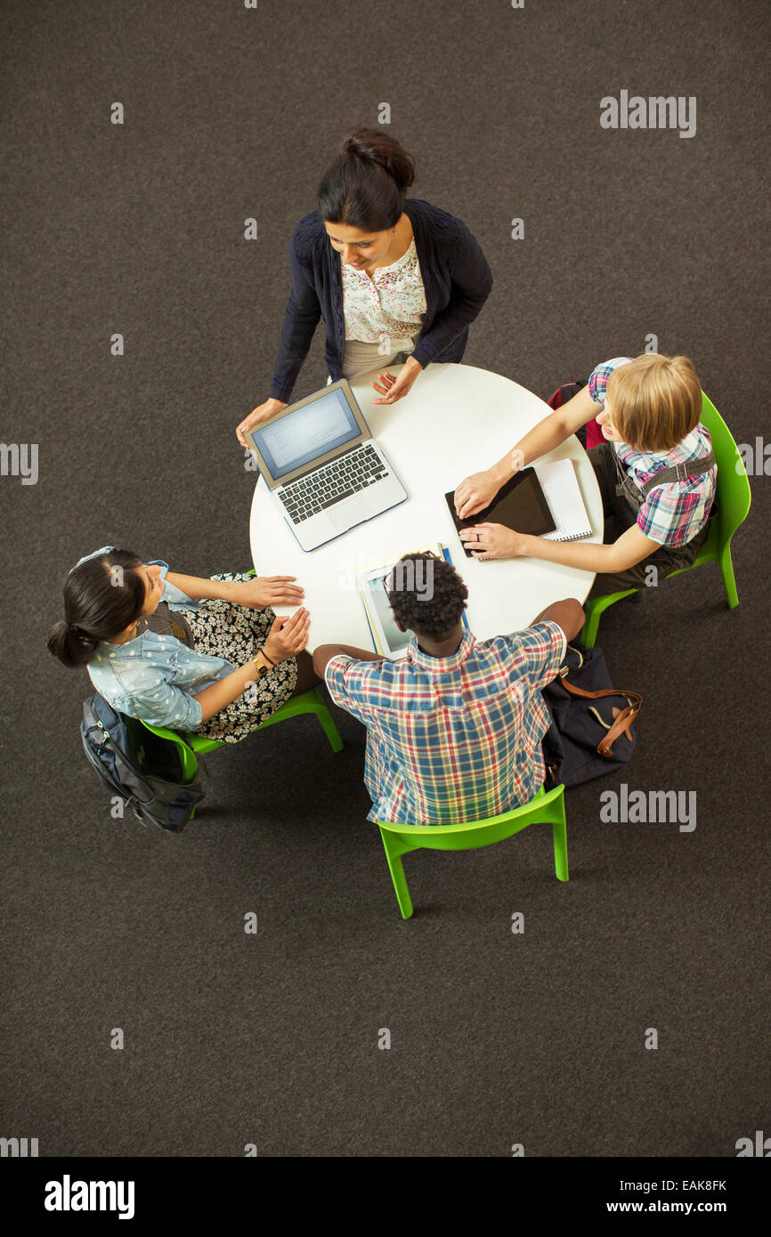 Overhead view of student doing homework at round table, using laptop and digital tablet Stock Photo