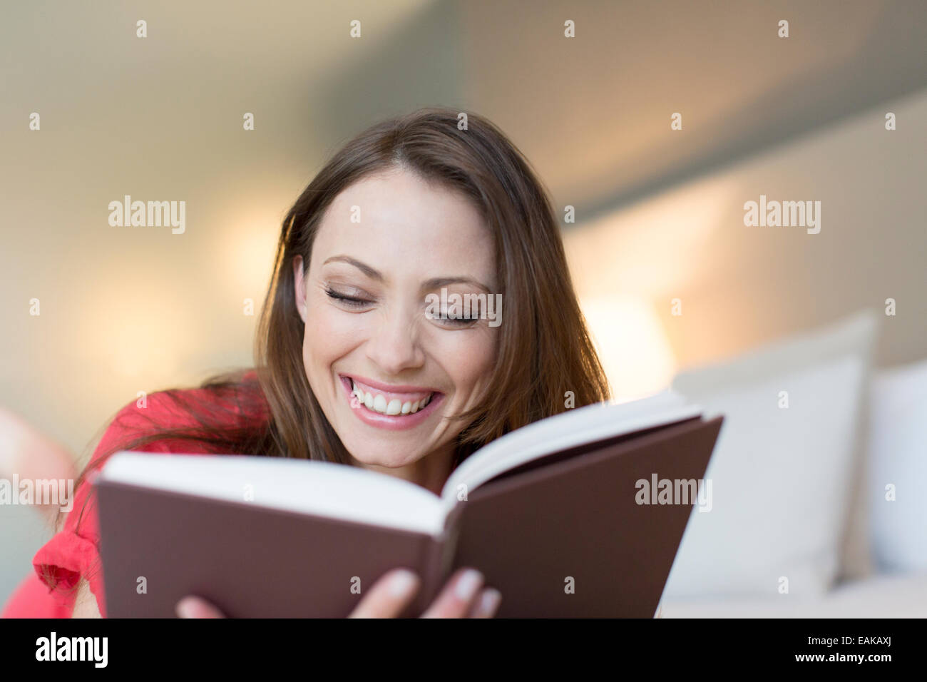 Smiling woman reading book in bedroom Stock Photo