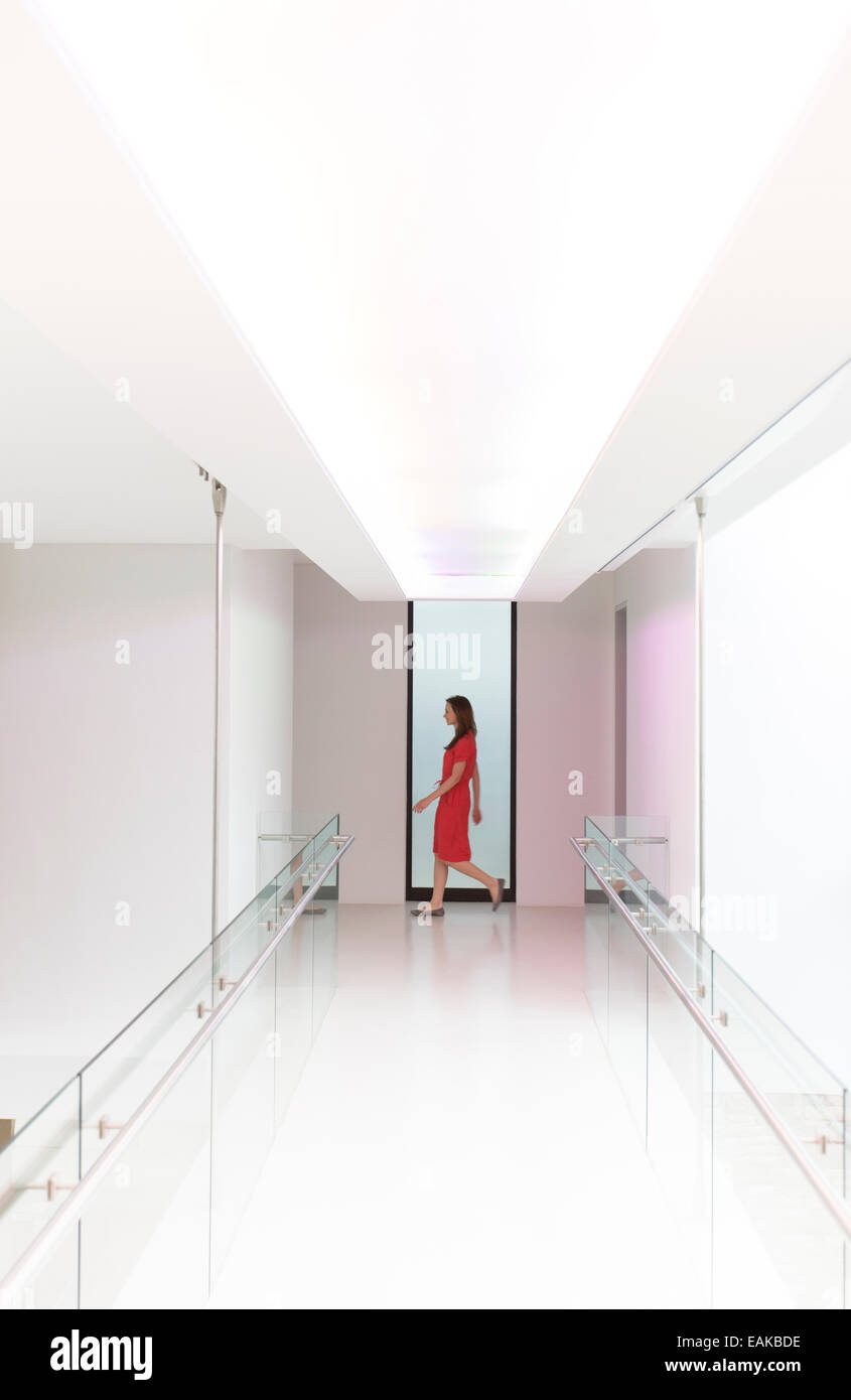 Woman in red dress walking through white modern corridor Stock Photo