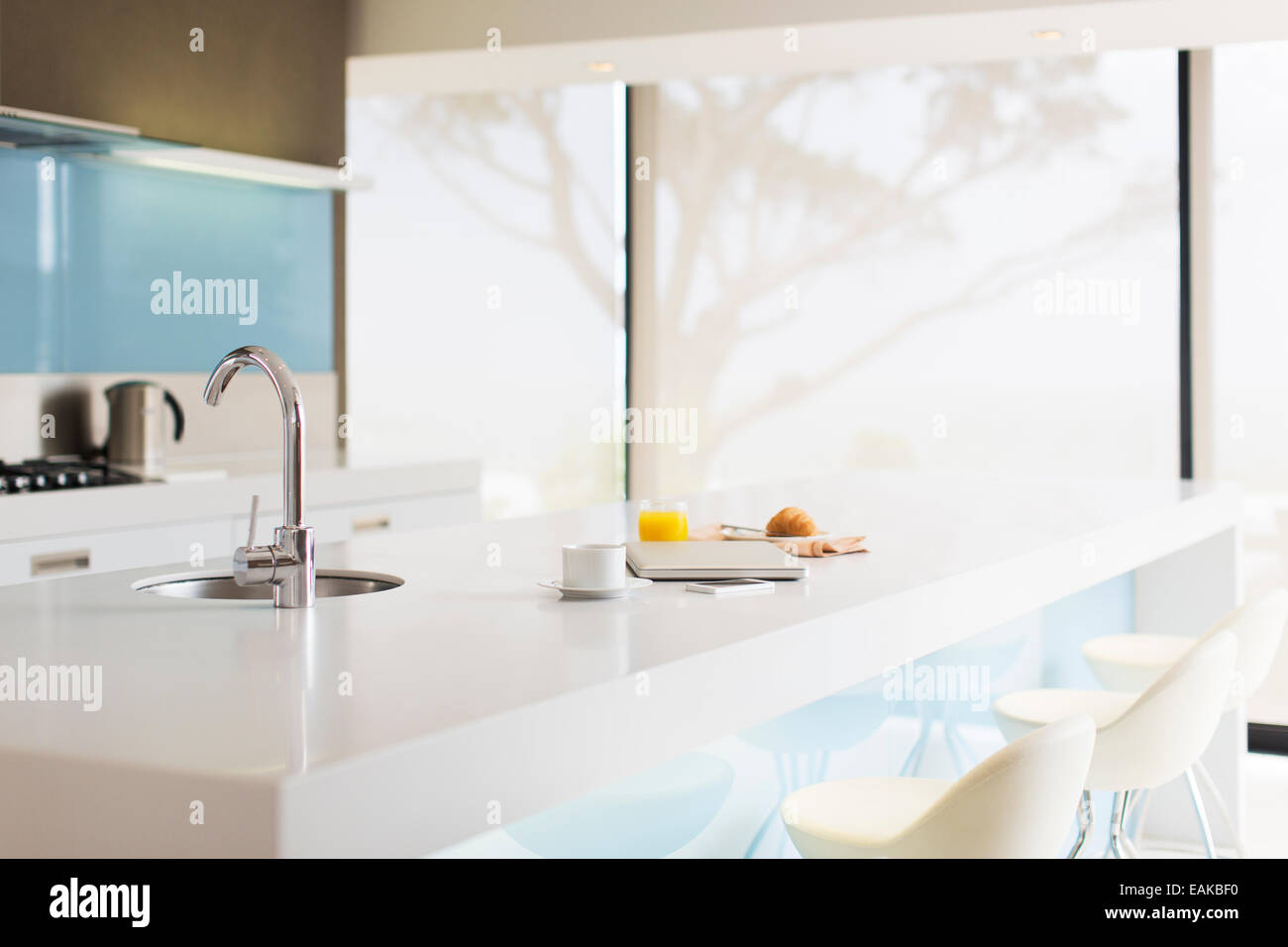 Laptop, coffee cup, glass of juice, croissant and newspaper on modern kitchen counter Stock Photo