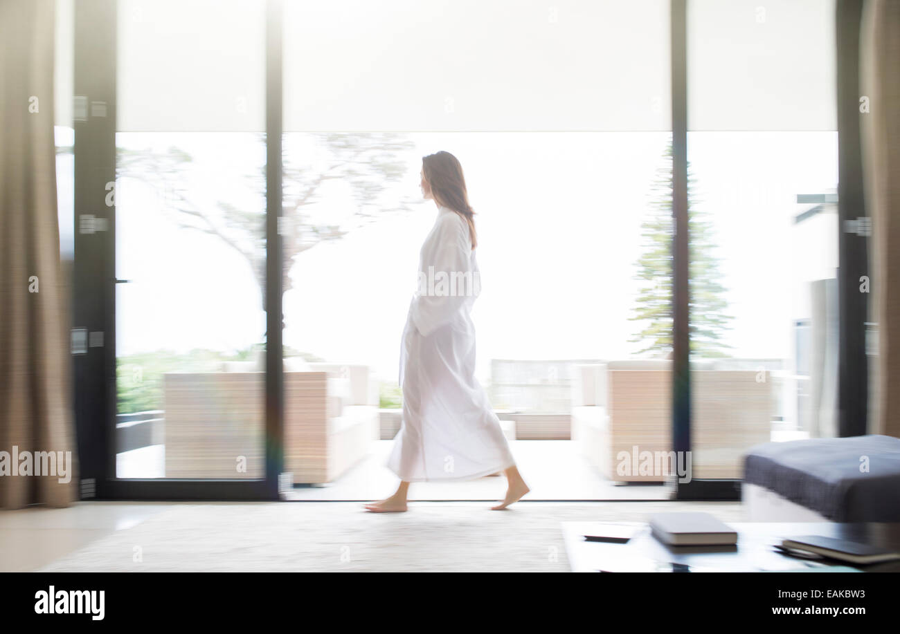 Woman in bathrobe walking through living room Stock Photo