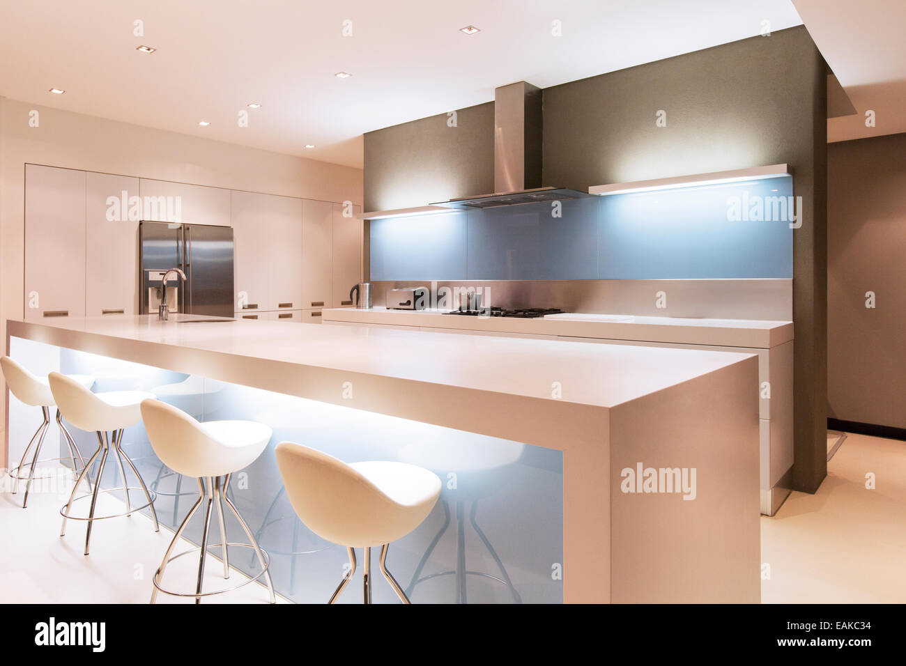 Modern white kitchen with kitchen island and stools illuminated at night Stock Photo