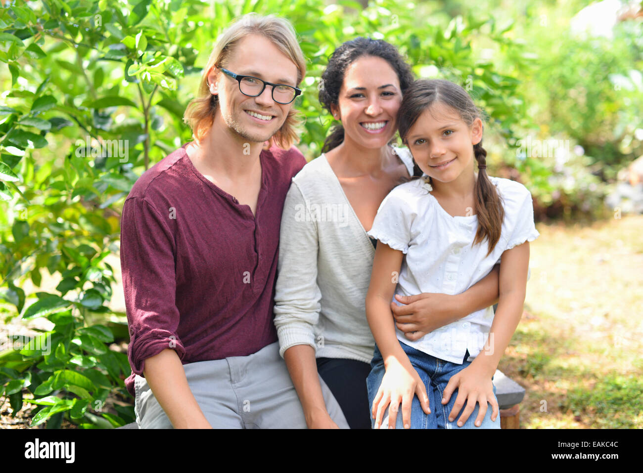 Portrait of smiling parents with daughter sitting on bench in garden Stock Photo