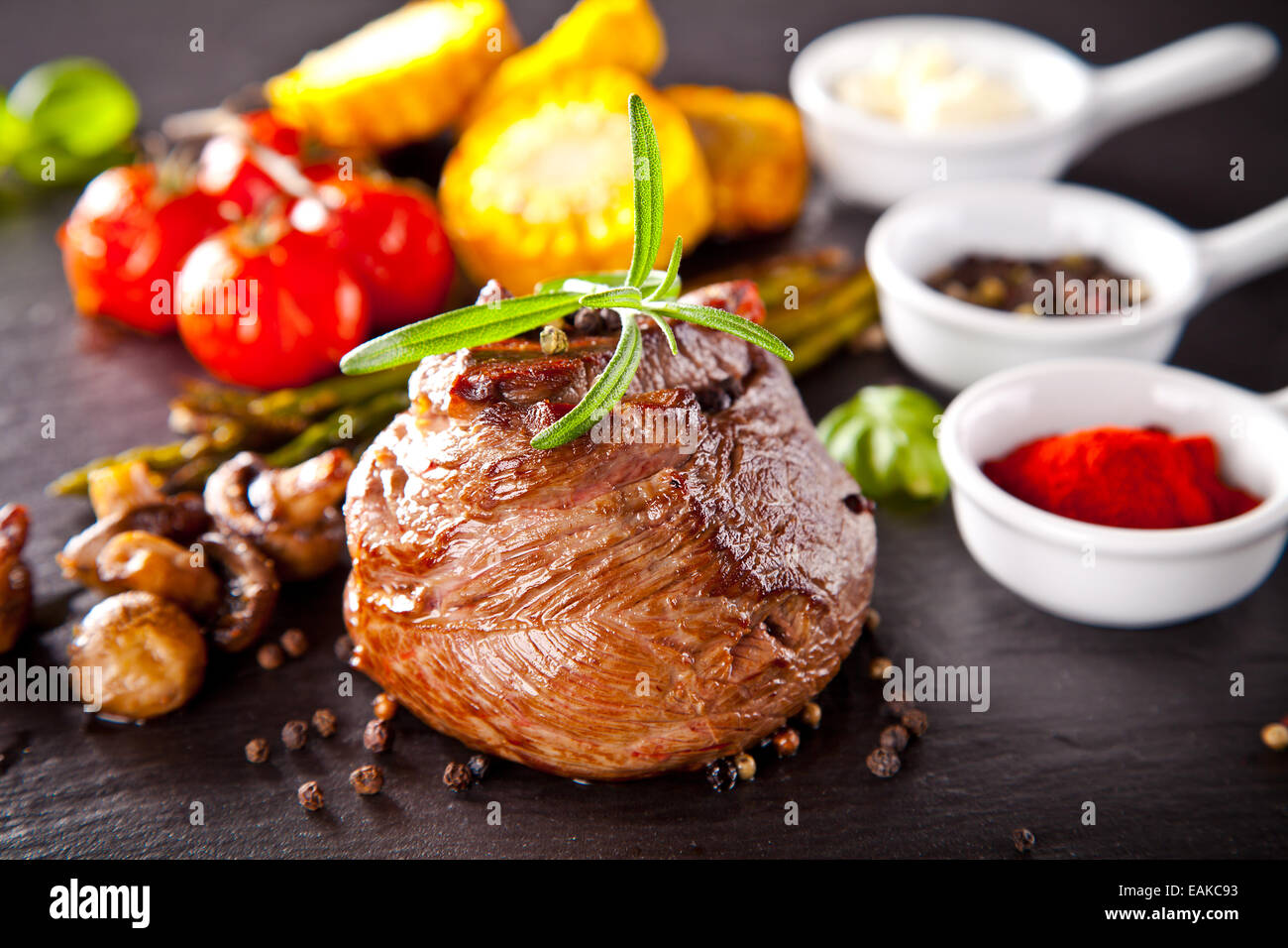Piece of red meat steak with rosemary served on black stone surface. Stock Photo