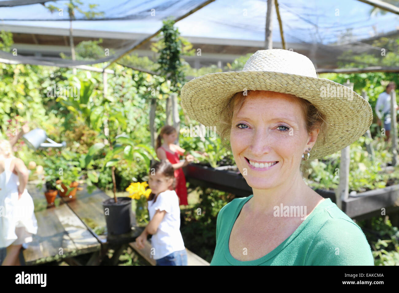 Portrait f smiling woman wearing sunhat in greenhouse, children in background Stock Photo