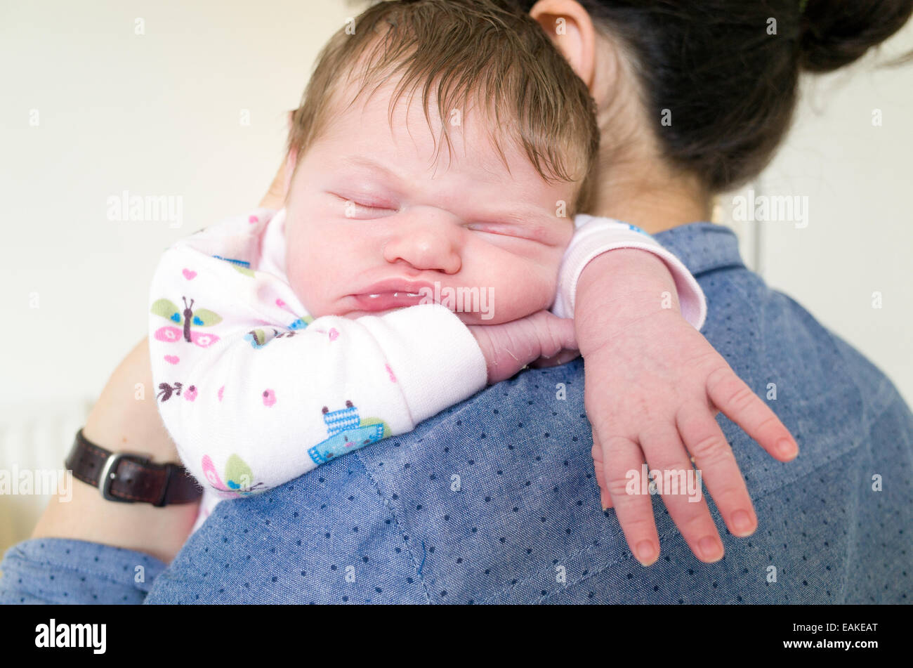 One week old newborn baby girl asleep on mothers shoulder Stock Photo