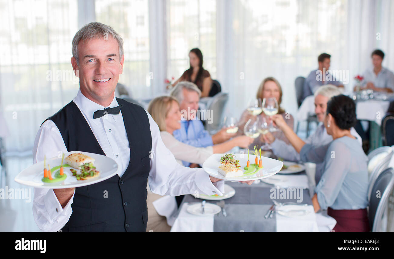 Portrait of waiter holding plate with fancy meals, people at restaurant