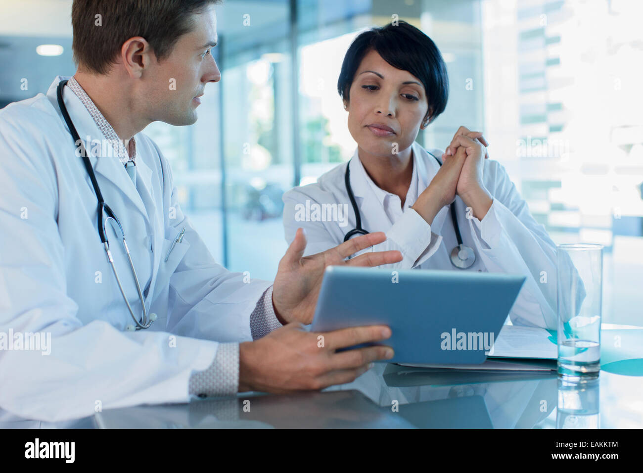 Doctors discussing patient's treatment at desk, using digital tablet Stock Photo