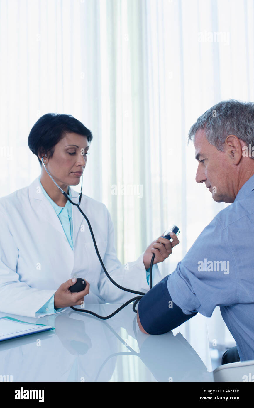 Female doctor taking patient's blood pressure at desk in office Stock Photo