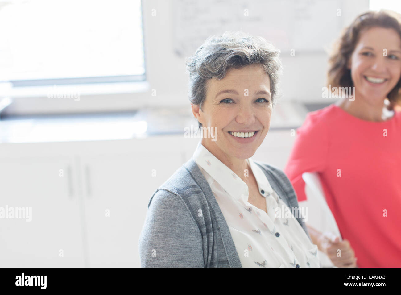 Portrait of smiling mature businesswoman with colleague in background Stock Photo