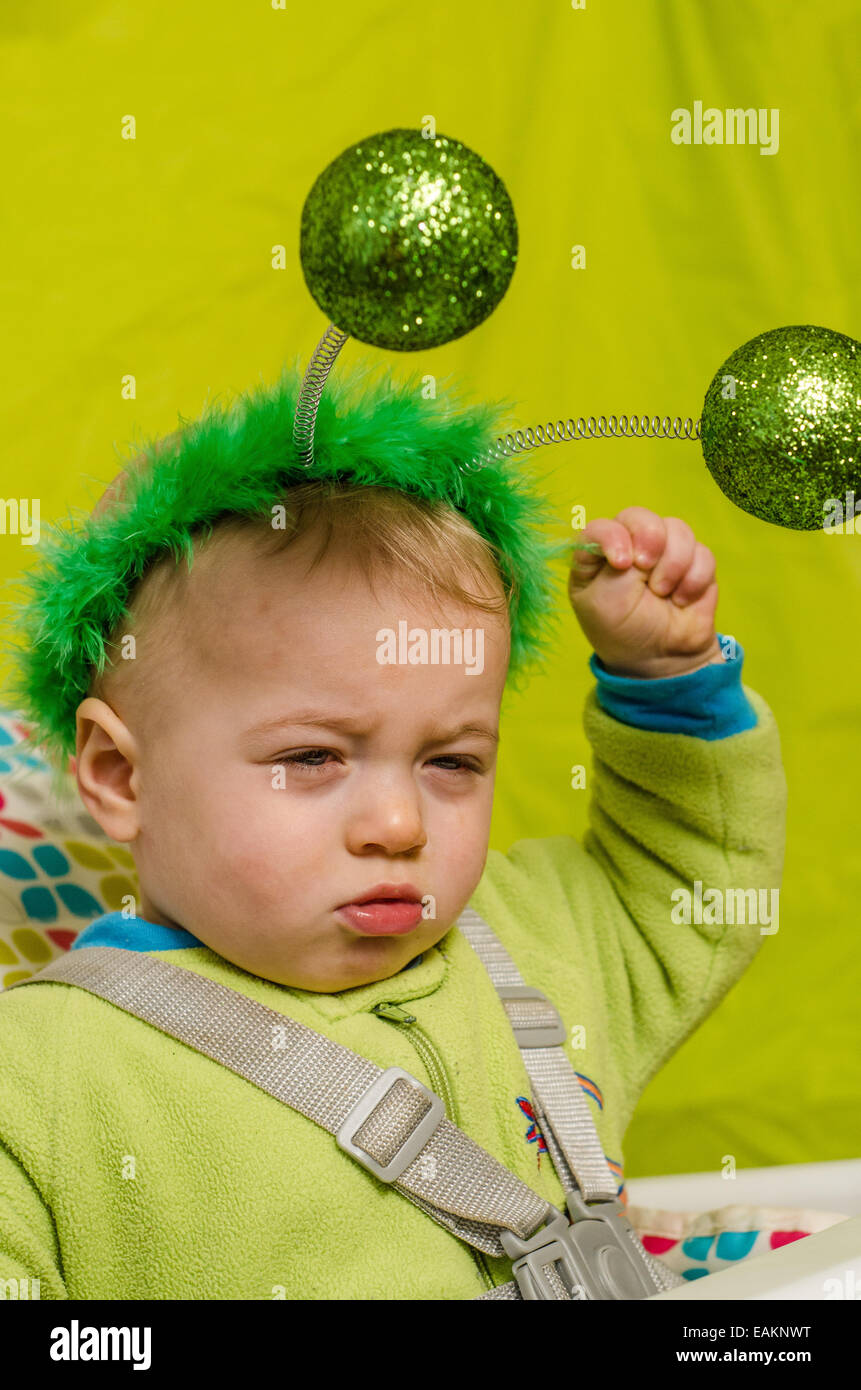 A baby boy (ca. 12 months old) wearing green joke antennae, and none too pleased about it. Stock Photo