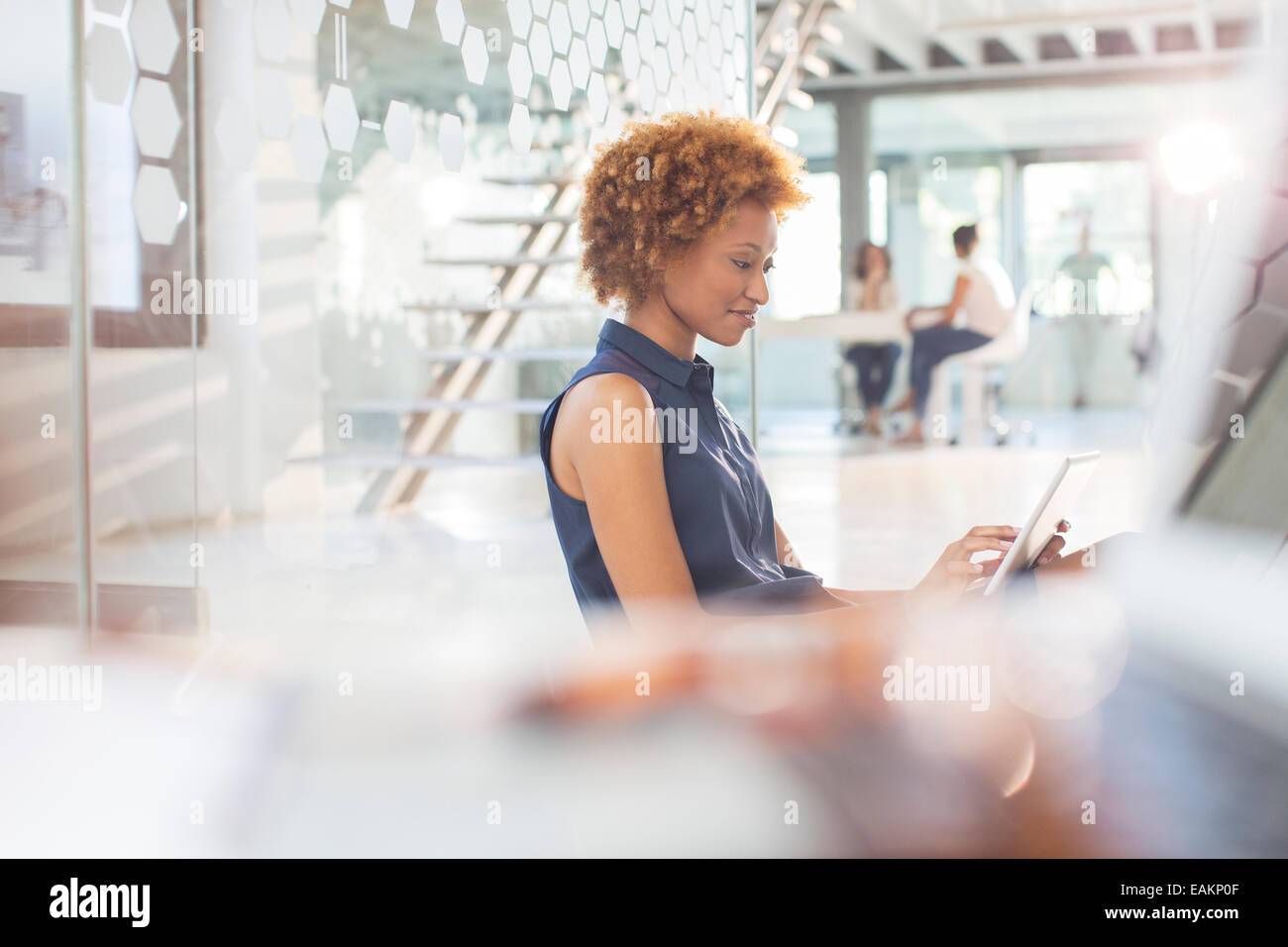 Woman using digital tablet in office, colleagues in background Stock Photo