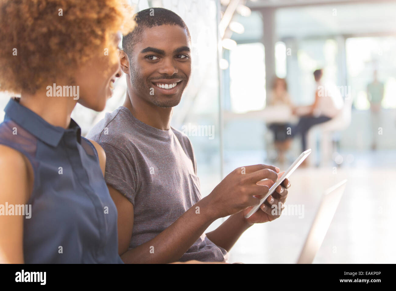 Man and woman using tablet in office, colleagues in background Stock Photo