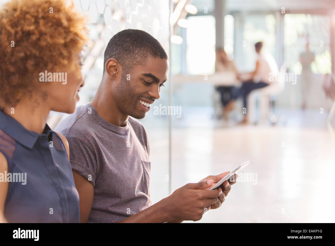 Man and woman using digital tablet in office, colleagues in background Stock Photo