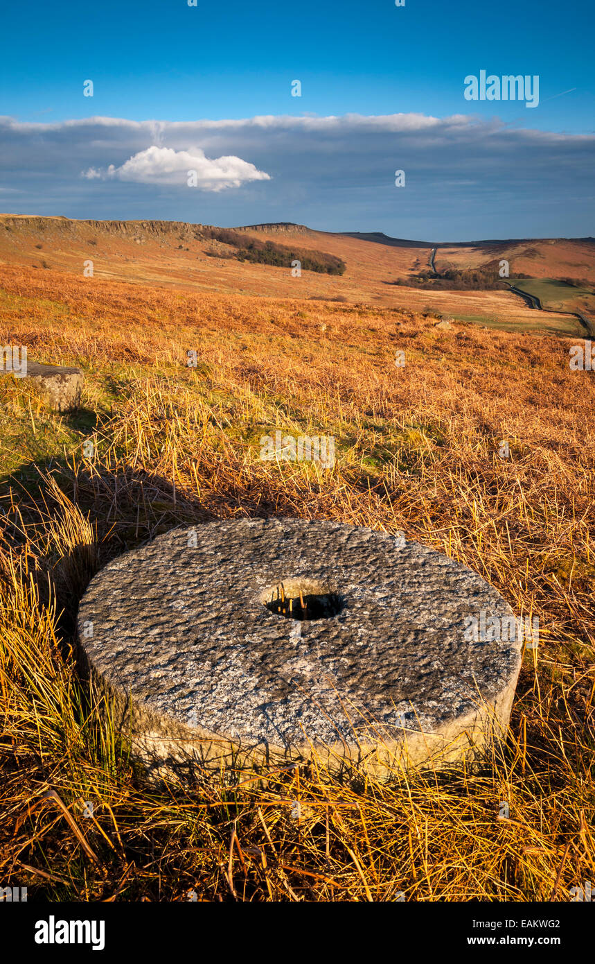 A lone millstone in the bracken below Stanage Edge in the Peak District, Derbyshire. Colourful moorland beyond. Stock Photo