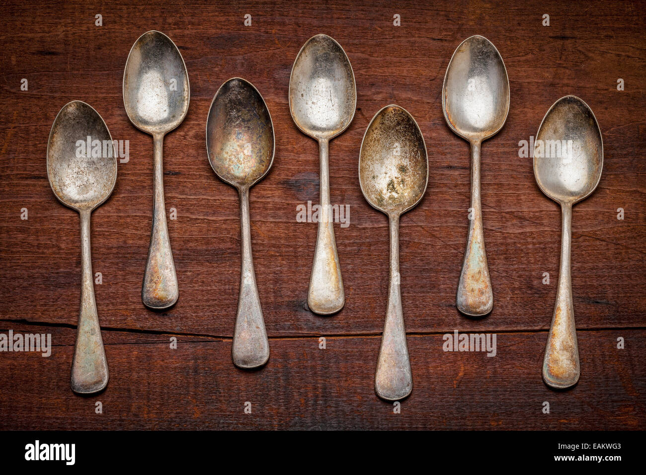 a row of vintage silver spoons with patina and scratches against grunge wood background Stock Photo