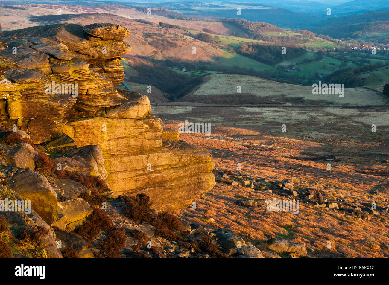View from Stanage Edge at dusk with golden glow on gritstone rocks. Village of Hathersage in the distance. Stock Photo