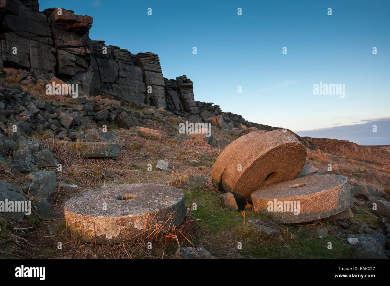Round millstones below Stanage edge in Derbyshire. Looking up beyond a group of stone to the dramatic gritstone escarpment. Stock Photo