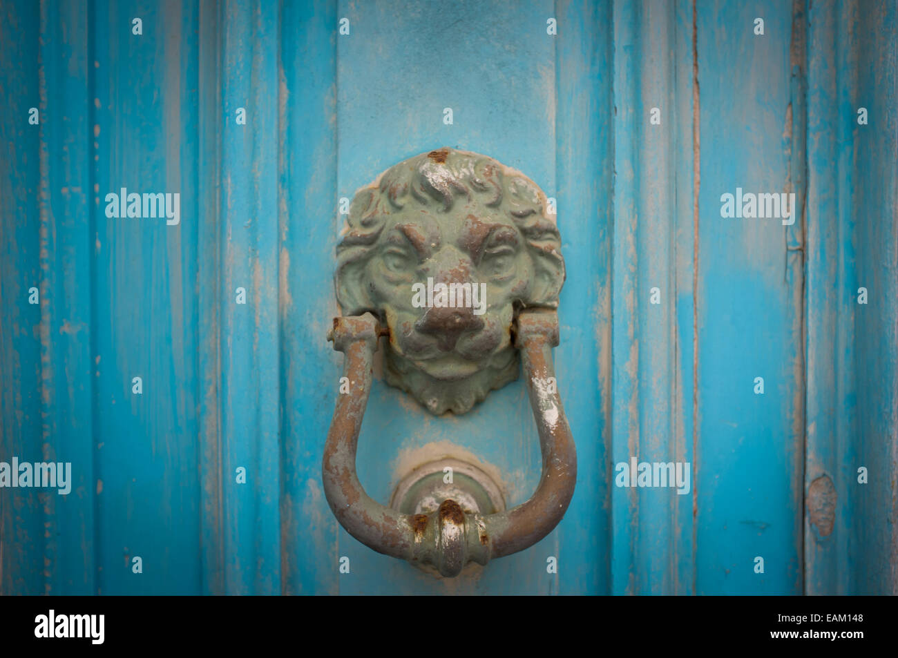 A rusty brass knocker on a weathered blue door in a coastal town in